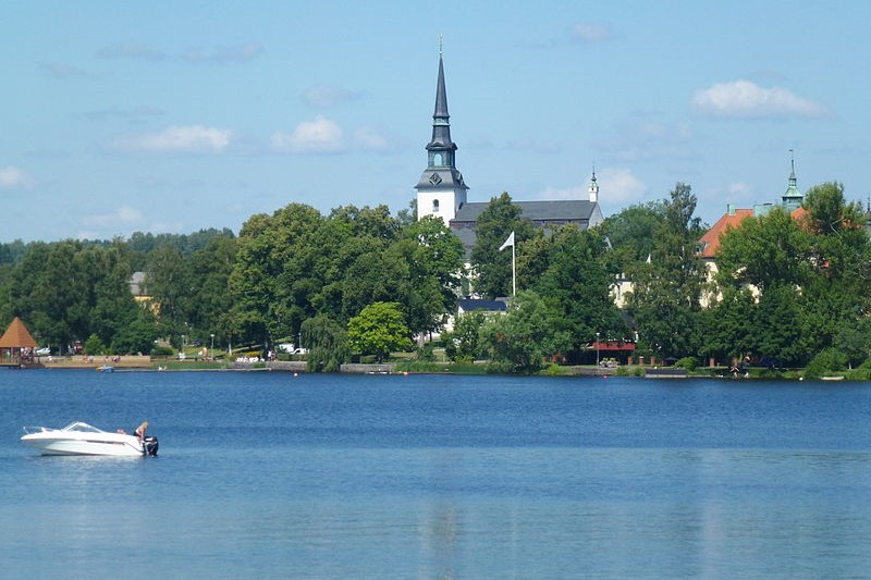 Träd skymmer kyrkan vid sjön i Lindesbergs kommun, där vi jobbar med trädfällning